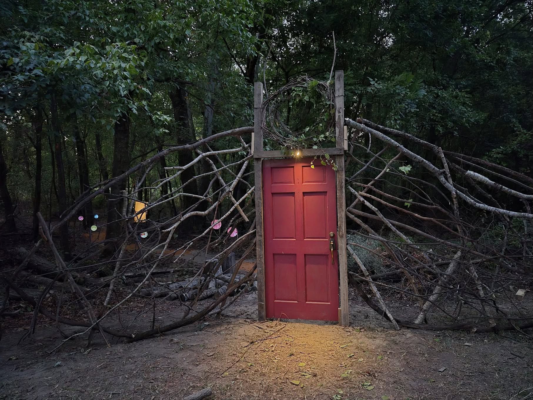 Red wooden door surrounded by intertwined branches along the Enchanted Forest trail at Lee Tartt Nature Preserve in Grenada, Mississippi.
